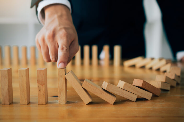 Close up finger businessman stopping wooden block from falling in the line of domino with risk concept.